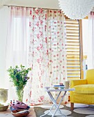 Summer bouquet in front of gauzy curtains with patterns of spots and roses combined with yellow armchair