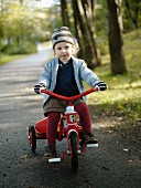 Kleines, blondes Mädchen mit gestreifter Mütze und Handschuhen, Dreirad fahrend auf einem Waldweg