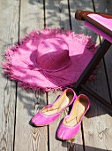 Pinkfarbene Ballerinas und Strohhut auf Holzterrasse vor Liegestuhl