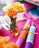 Aufgerollte Tischsets neben gelbem Blumenstrauss auf pinkfarbener Tischdecke