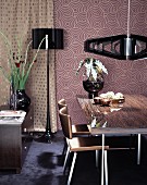 Dining table and chairs below designer pendant lamps against retro wallpaper