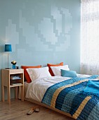 Double bed with striped bedspread and modern bedside cabinet against blue wall