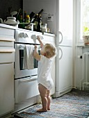 Kleines Kind im Bodyanzug steht am Küchenherd