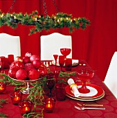 Festively set table and white upholstered dining chairs in front of red curtain