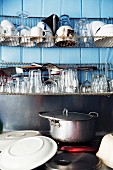 Glasses and cups on metal drying rack above pans on cooker