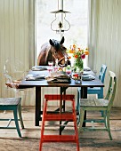 Farbig angestrichene Holzstühle um gedeckten Tisch und neugieriges Pferd schaut durch offenes Fenster herein