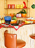 Counter along wall below retro-look bamboo shelves; blue fondue set and forks on burner on counter