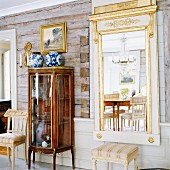 Antique glass display case and gilt-framed mirror on rustic wall of log cabin
