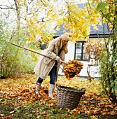 Young woman raking up leaves in autumnal garden