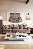 Framed, ethnic garment above precisely arranged cushions in ethnic patterns on grey couch in modern living room; wooden collectors' items on coffee table