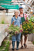 Frau und Mann mit Arbeitskleidung und Blumenapmel in Hand im Gartencenter