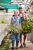 Young woman and mature man walking with hanging baskets in garden centre