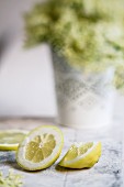 Lemon slices on a wooden table; elderflowers in the background