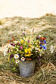 Bouquet of wild flowers in old bucket amongst hay