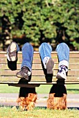 Two girls hanging upside down on wooden bench