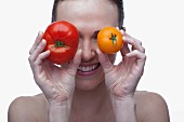 Young woman covering eyes with red and yellow tomato