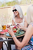 Drei ältere Damen essen Obstsalat an Tisch im Freien