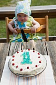 Baby schaut auf den Geburtstagskuchen auf Gartentisch