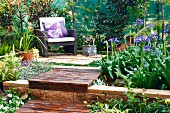 Sonniger Platz mit gemütlichem Sessel und integrierte Blumenbeete auf Terrasse im Garten