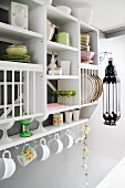 Crockery on open-fronted kitchen shelves and cups hanging from hooks below