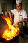 Chinesischer Koch mit brennendem Öl im Wok