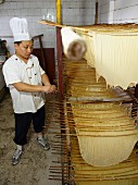 A Chinese chef standing next to drying tofu skins