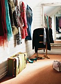 Various scarves hanging from coat pegs and vintage suitcase in front of valet stand next to wall mirror in wood-panelled dressing room