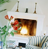 Amaryllis in glass vase on table and striped armchair in front of open fire
