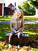 Girl sitting on wooden crate in autumnal garden