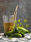 Fresh pickling cucumbers with dill flowers and a measuring jug with vinegar