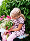 Kleines Mädchen mit pinkfarbenem Blumenstrauss auf einer Holzbank sitzend