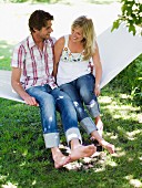 Junges, lachendes Paar auf Hängematte im sonnigen Garten