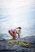 Aus Pflanzengrün gelegtes I-love-you auf einem Felsen; im Hintergrund Mädchen am Wasser