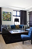 Blau bezogener Sessel mit gedrechselten Füssen und Couchtisch vor Sofa, seitlich eine Bogenlampe in Wohnzimmerecke