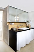 Broad, mirrored cabinet above orange mosaic tiles and black-painted washstand with white curtain