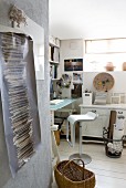 Modern barstool at desk with glass top and white, shabby-chic cabinet in home office; tattered poster in foreground