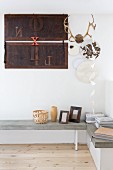 Stacked magazines and small ornaments on concrete corner bench below decorative plates, antlers and collage of letters on wall