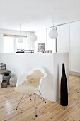 Large, black decorative bottle and classic shell chair with sheepskin rug in front of half-height, masonry wall element and spherical lamps