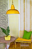 Holztisch mit Zimmerpflanze, gelber Stuhl und gelbe Hängelampe vor Tapetenbahnen
