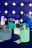 Various paints in glass jars on length of blue patterned wallpaper