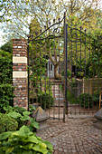Geöffnetes schmiedeeisernes Gartentor mit Backstein- Mauerpfeiler und Blick zu idyllischem Gartenhäuschen