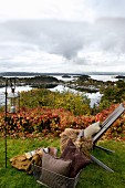 Gartenstuhl mit Felldecken, Kissen und Windlicht in herbstlichem Garten mit Blick auf die norwegische Schärenküsten