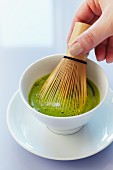 Matcha tea being stirred with a bamboo whisk