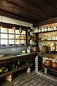 Ceramic pots and white crockery on shelves mounted on brick walls in rustic kitchen