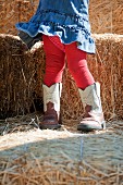 Kleines Mädchen mit großen Cowboystiefeln auf Strohballen