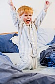 Kleiner Junge mit Rotschopf morgens tobend im Elternbett