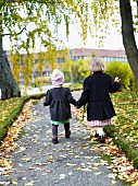 Zwei Kinder in Wintermänteln gehen Hand in Hand Weg entlang
