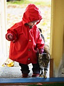 Toddler in raincoat & cat walking into house