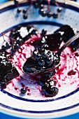 A spoon of elderberry jam and elderberries on a plate