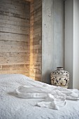 Double bed with white bedspread and urn against exposed concrete wall